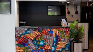 A reception desk with a colorful mosaic design, a flat-screen TV, and a potted plant. - ONOMO Hotel Maputo (Maputo)