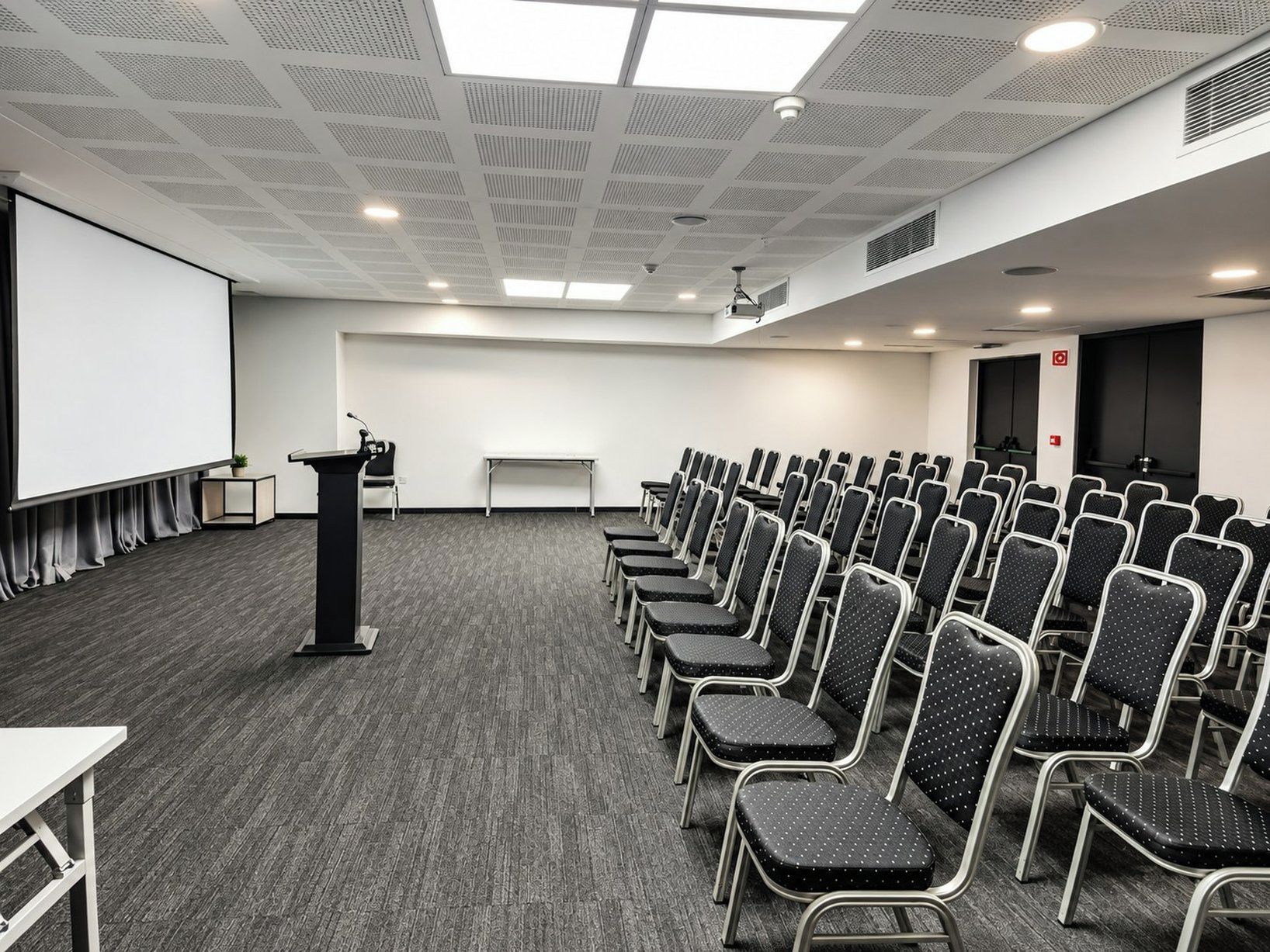 A conference room with rows of chairs, a podium, a projector screen, and a whiteboard.