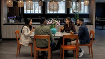 A group of people seated at a table in a modern dining area with pendant lighting and a view of the kitchen in the background.