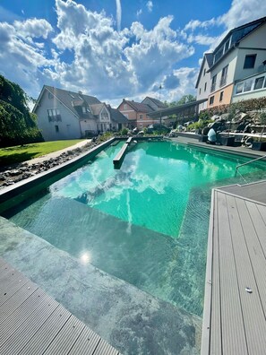 A swimming pool with clear water, surrounded by a wooden deck, and adjacent to residential buildings. - Category C: Double Room - Inn - Pension - Drei Linden (Pegnitz)