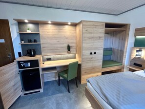 Una habitación de hotel compacta con un escritorio de madera, una silla verde, una cama y un armario.