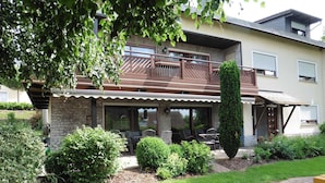 A two-story house with a balcony, a patio with outdoor furniture, and a well-maintained garden.