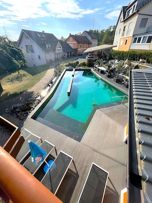 Une piscine dotée d’une terrasse en bois, de chaises longues et offrant une vue sur les bâtiments environnants.