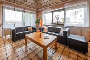 Ein modernes Wohnzimmer mit einer Couch, einem Holztisch und großen Fenstern.
