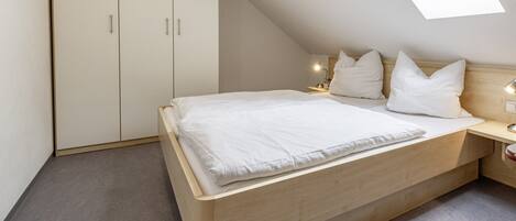 A bedroom with a bed, a wardrobe, a bedside table, and a skylight.