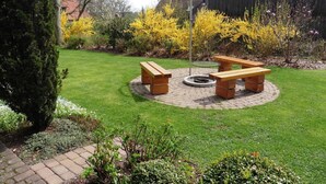 A circular outdoor seating area with benches and a fire pit, surrounded by a well-maintained lawn and flowering shrubs.