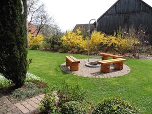 A circular outdoor seating area with benches and a fire pit, surrounded by a well-maintained lawn and flowering shrubs. - Category C: Double Room - Inn - Pension - Drei Linden (Pegnitz)