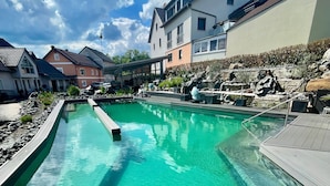 A swimming pool with clear water, surrounded by a wooden deck and a rock garden.