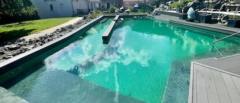 A swimming pool with clear water, surrounded by a wooden deck, and adjacent to residential buildings.
