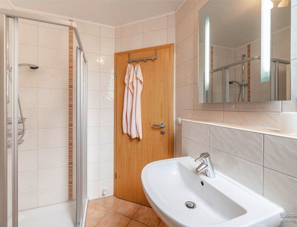 Ein Badezimmer mit Dusche, Waschbecken, einer Holztür und einem Spiegel.