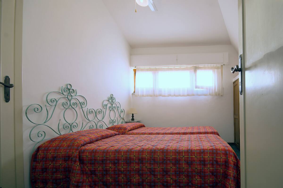 A bedroom with two beds, a window with curtains, and a metal headboard.