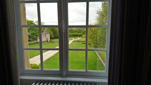 A window with a view of a well-maintained garden and a small stone building. - Manoir de Conjon (Crouay)