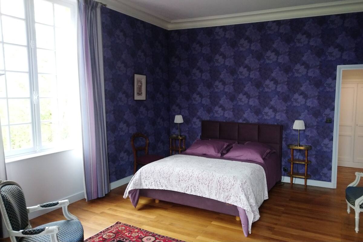 Un dormitorio con una cama, dos mesitas de noche, una silla y una puerta.