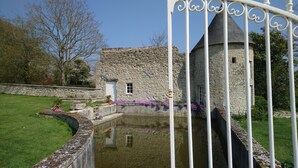 A stone building with a conical roof, a small window, and a door. There is a white metal fence in the foreground. - Manoir de Conjon (Crouay)