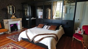 A bedroom with a large bed, a fireplace, a mirror, and a red armchair. - Manoir de Conjon (Crouay)