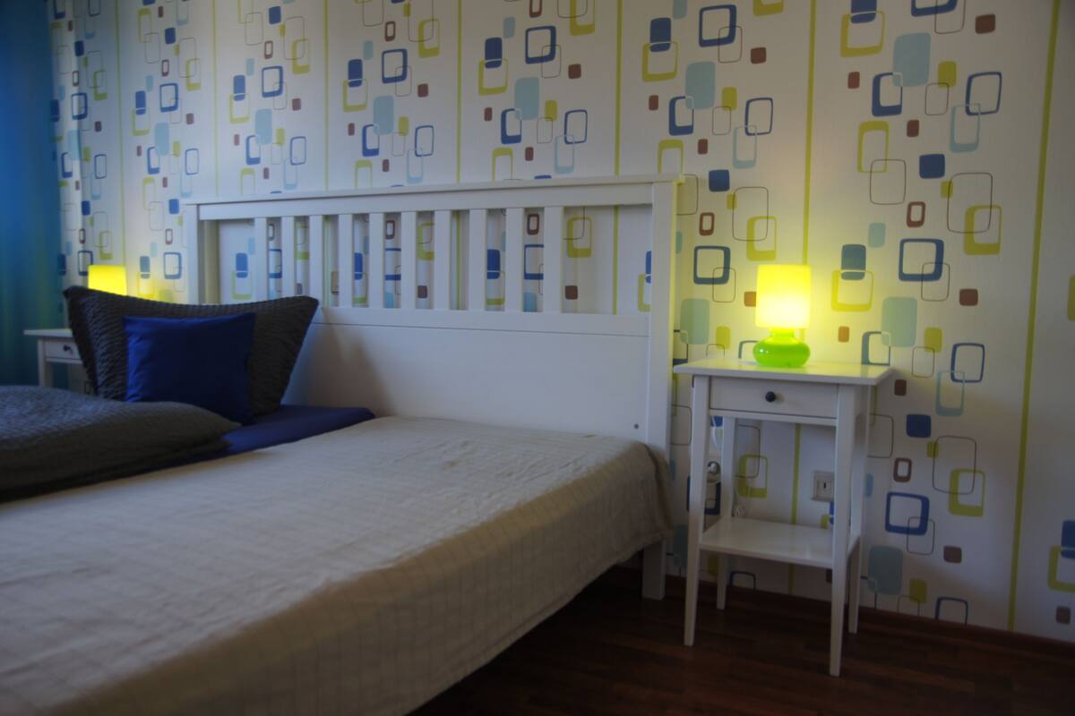 A bedroom with a bed, bedside table, and a wall with a geometric pattern.