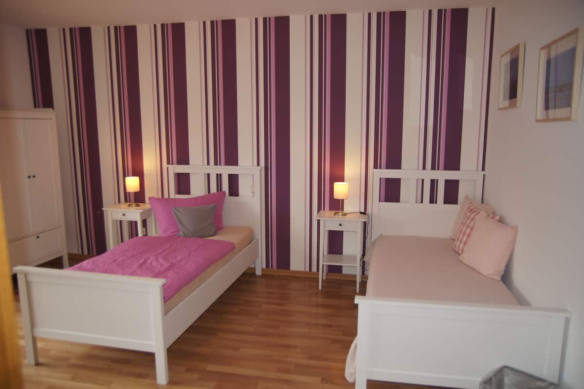 A bedroom with two beds, a wardrobe, and striped wallpaper.