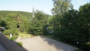 A parking area with a view of a church steeple and surrounding greenery. - Gasthof Schumacher - Hotel garni (Freudenberg)