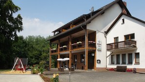 A two-story building with a balcony, a sign indicating it is a hotel, and outdoor seating. - Gasthof Schumacher - Hotel garni (Freudenberg)