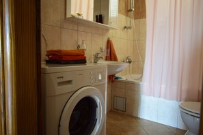 A compact bathroom with a washing machine, a sink, and a shower.