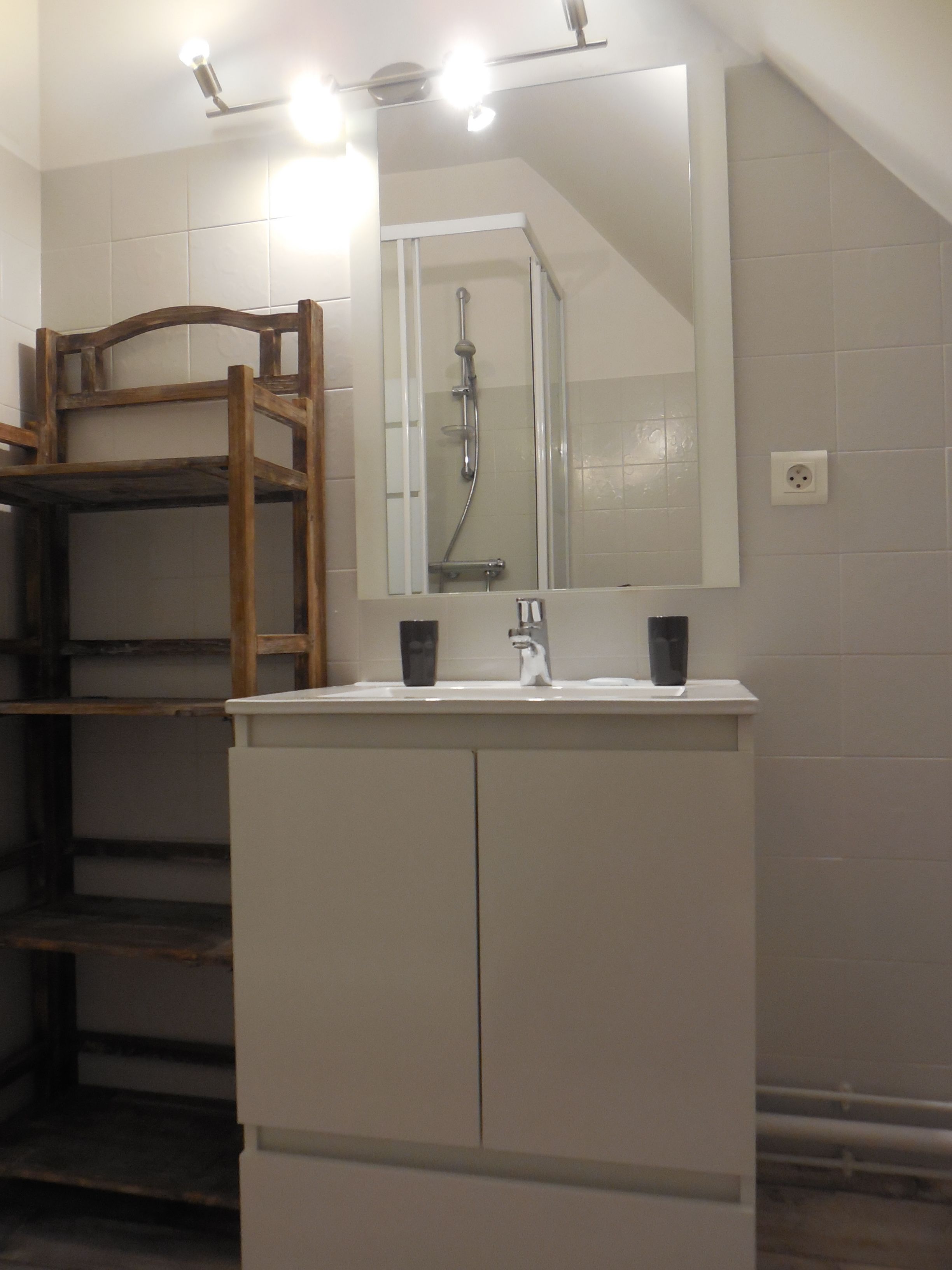 Ein Badezimmer mit Waschbecken, Spiegel und Dusche. Eine hölzerne Bank befindet sich links.