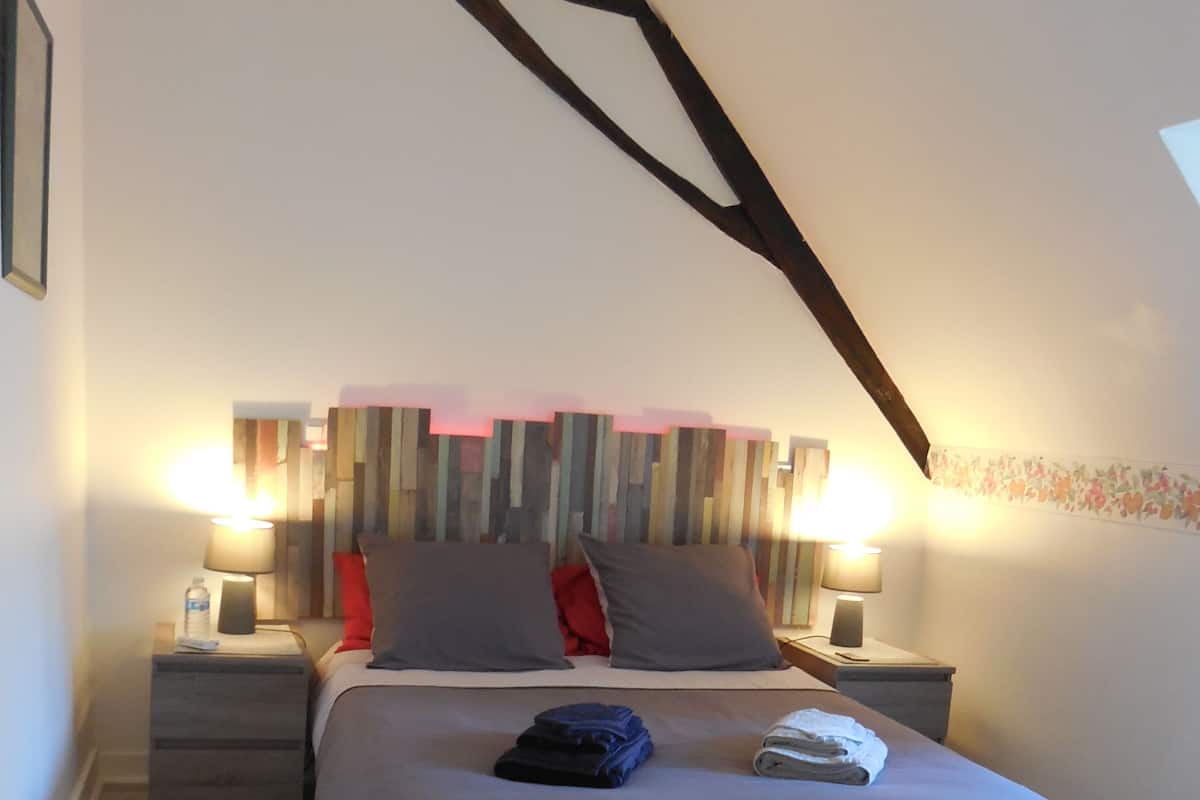Um quarto com uma cama, duas mesas de cabeceira, uma luminária e piso de madeira.