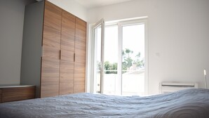 A bedroom with a large bed, wooden wardrobe, and a sliding glass door leading to a balcony.