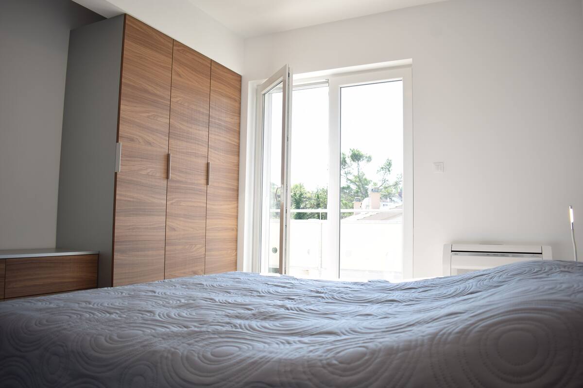 A bedroom with a large bed, wooden wardrobe, and a sliding glass door leading to a balcony.