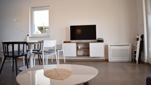 A modern living room with a flat-screen TV, white furniture, and a large window.