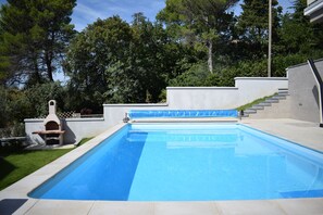 Una piscina rectangular con superficie de agua azul cristalina, rodeada por un deck de concreto y un muro bajo de piedra.