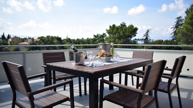 A wooden table and chairs on a balcony with a clear view of trees and buildings in the background.