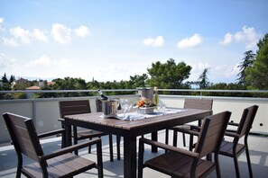 Une table et des chaises en bois sur un balcon, offrant une vue dégagée sur les arbres et les bâtiments en arrière-plan.