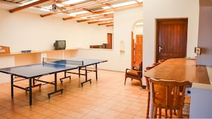 A room with a ping pong table, wooden chairs, a small television, and a wooden cabinet. - Addo Park View - Sundaze Riverside (Colchester)