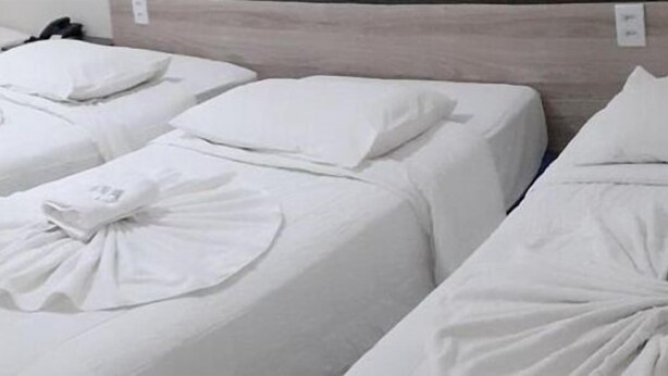 A hotel room with three neatly made beds, each with a pillow and a towel arranged in a decorative manner.