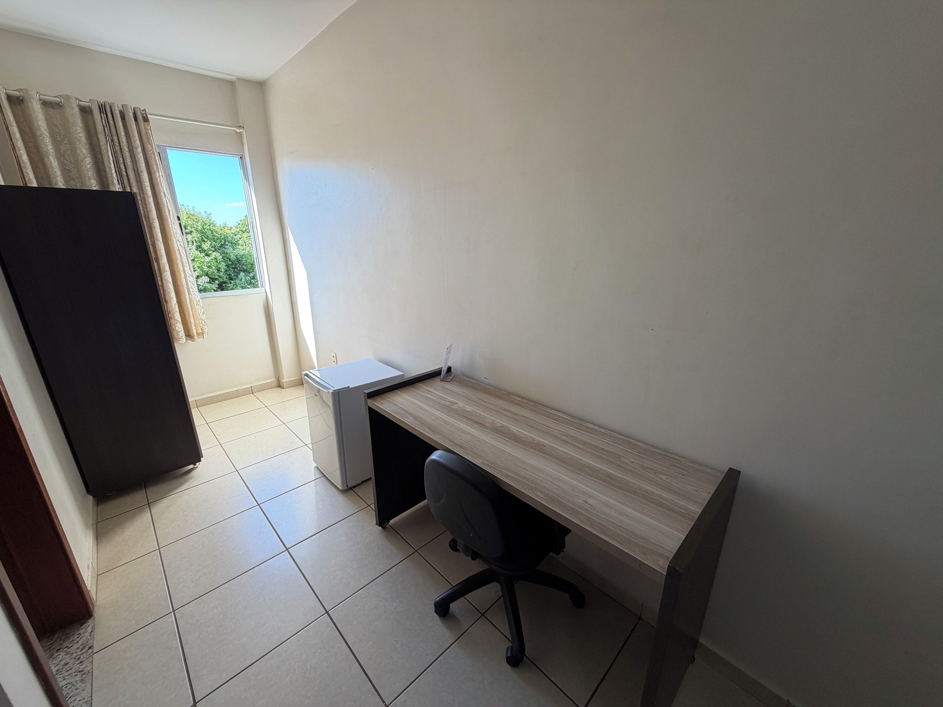 Un pequeño espacio de oficina con escritorio, silla y ventana con cortinas.