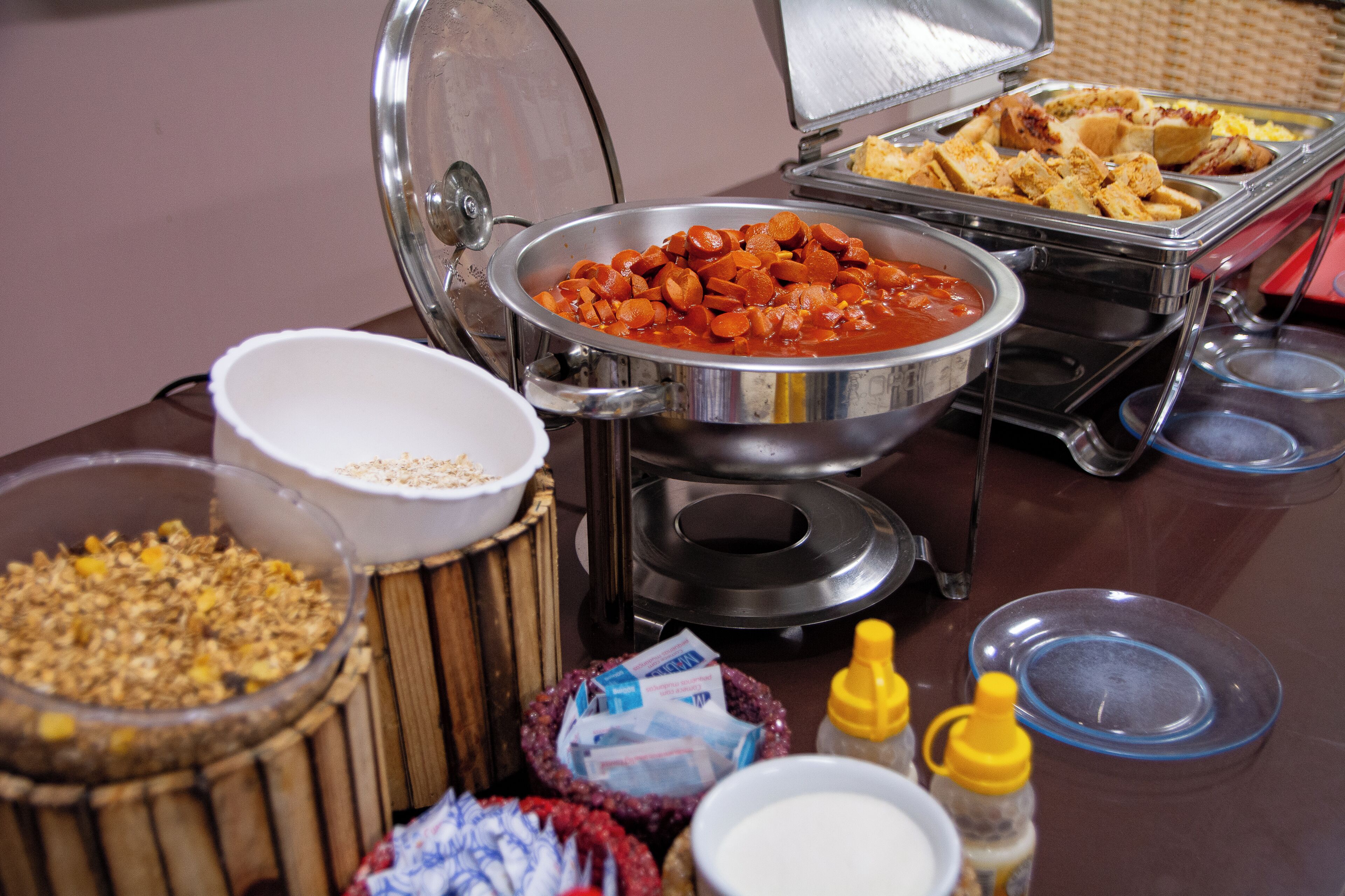 Ein Buffet mit verschiedenen Speisen, darunter eine Schüssel mit roter Soße, eine Schale mit Granola und mehrere Flaschen mit Soßen.