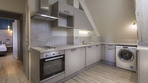 Une cuisine compacte équipée d’un four encastré, d’un lave-linge et d’un petit coin repas avec une table et des chaises.