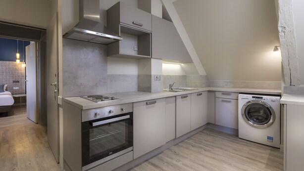 A compact kitchen with a built-in oven, a washing machine, and a small dining area with a table and chairs. - Demeure des Remparts (Provins)