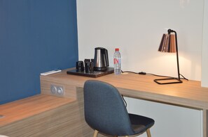A modern hotel room with a wooden desk, a chair, a coffee maker, a water bottle, a remote control, and a lamp. - Demeure des Remparts (Provins)