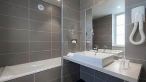 Une salle de bain moderne équipée d’une baignoire, de deux lavabos, d’un miroir et d’un sèche-mains.
