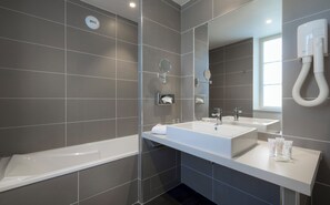 Un baño moderno con bañera, dos lavamanos, un espejo y un secador de manos.