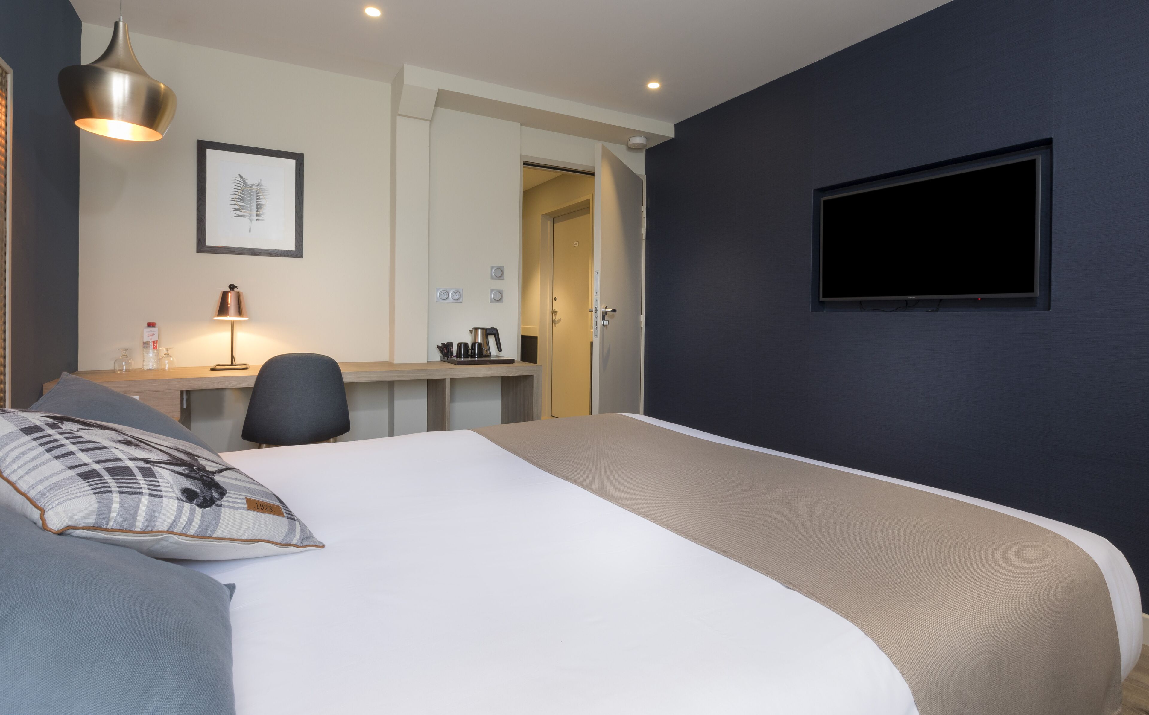 Une chambre d’hôtel avec un lit, un bureau, une chaise, une télévision et un tableau encadré au mur.