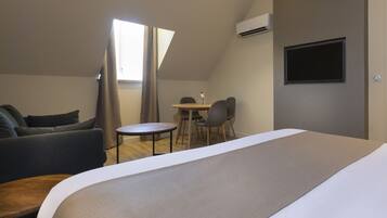 A modern hotel room with a large bed, a sofa, a small round table, and a TV mounted on the wall.