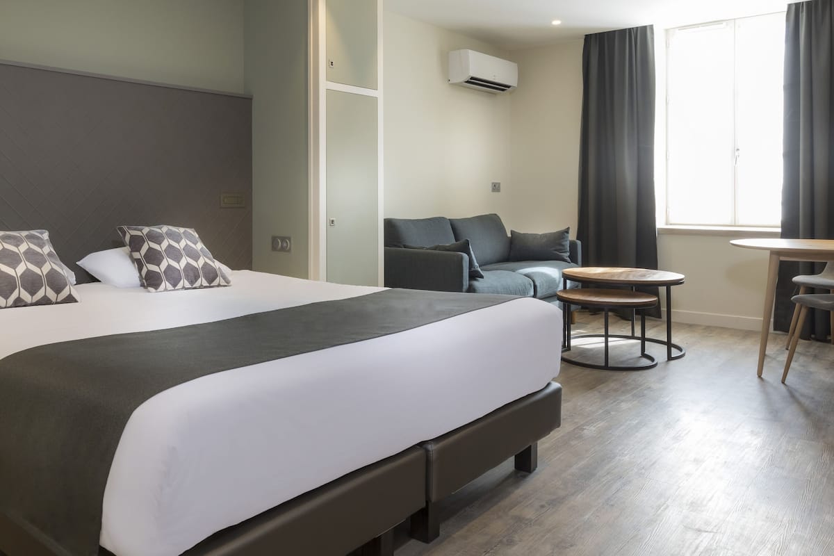 Una habitación de hotel con una cama grande, un sofá, una mesita con sillas y una ventana con cortinas.