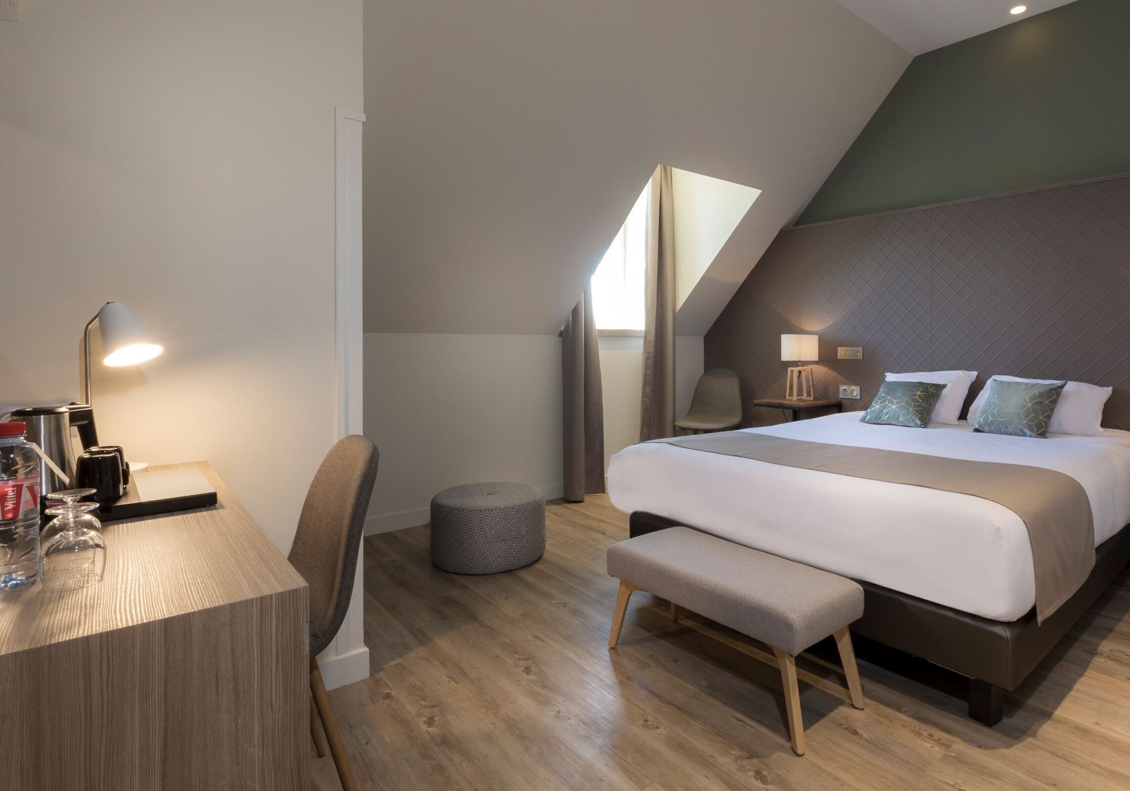 A modern bedroom with a bed, bedside table, lamp, and a small stool.