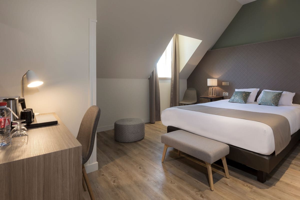 Un dormitorio moderno con cama, mesita de noche, lámpara y un pequeño taburete.