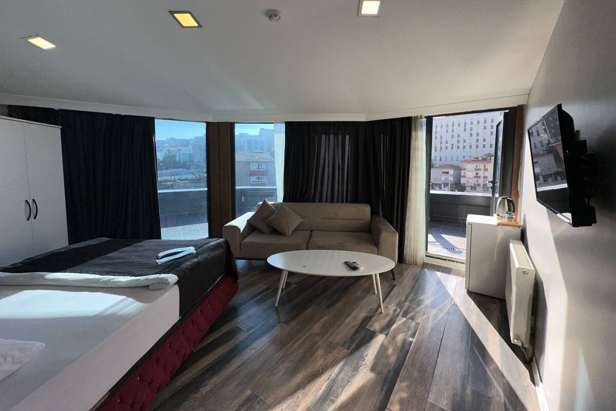 A modern hotel room with a bed, a sofa, a coffee table, and a TV.