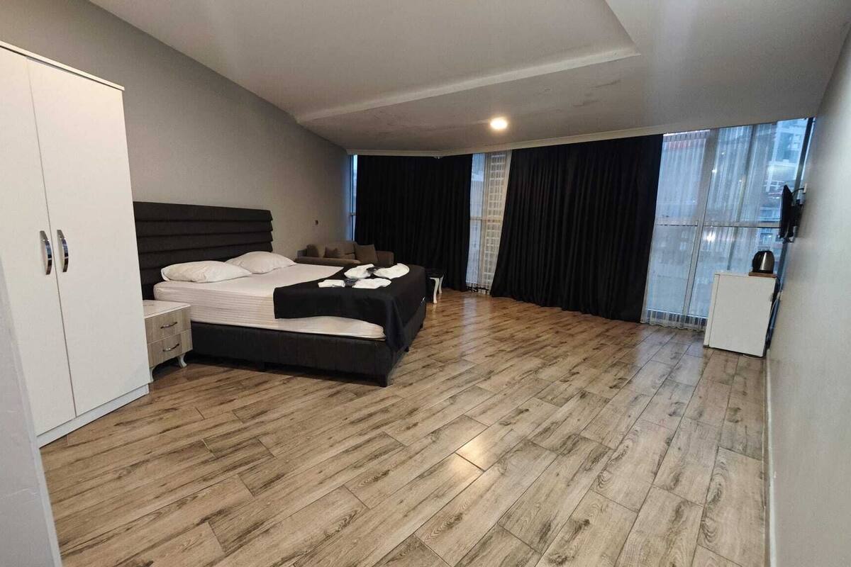 A modern bedroom with a large bed, a wardrobe, and a small kitchenette.