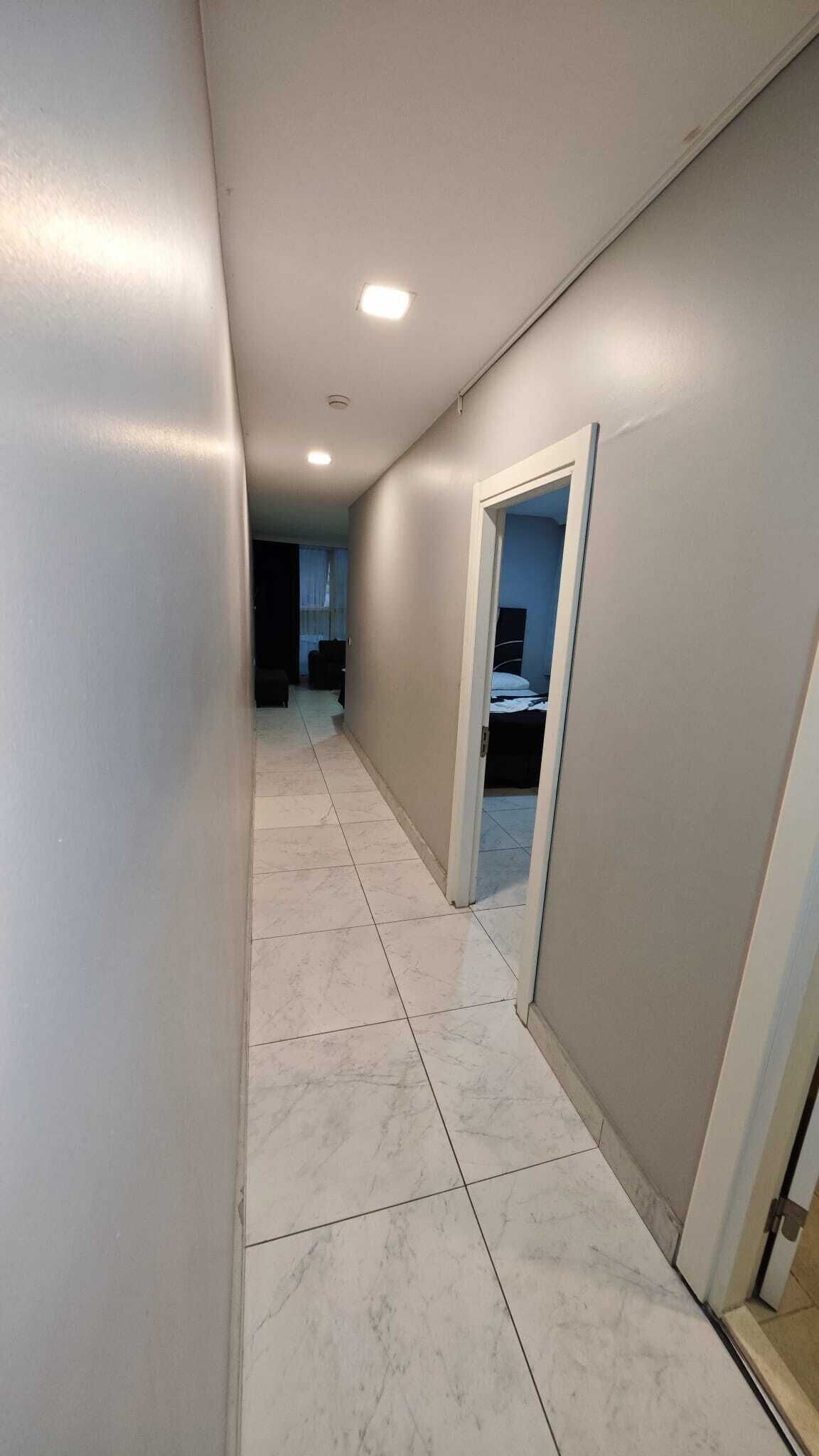 A hallway with a tiled floor, a door leading to a room, and a ceiling with recessed lighting.