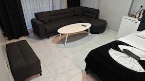 Una habitación de hotel moderna con sofá, una pequeña mesa de centro, cama y escritorio con computadora.
